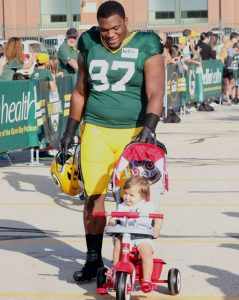 Defensive tackle Kenny Clark, the Packers' first-round draft choice out of UCLA, pushes a younger on her three-wheeler on his way to practice July 30. Greg Seubert Photo