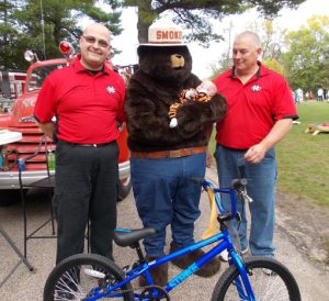 Decklin Larsen, of Omro, won a bicycle at last year's Firefest, sponsored by the Manawa Rural Fire Department. Presenting the bicycle were (from left) MRFD Assistant Chief Josh Smith, Smokey Bear and Fire Chief Rob Rosenau. Jane Myhra Photo